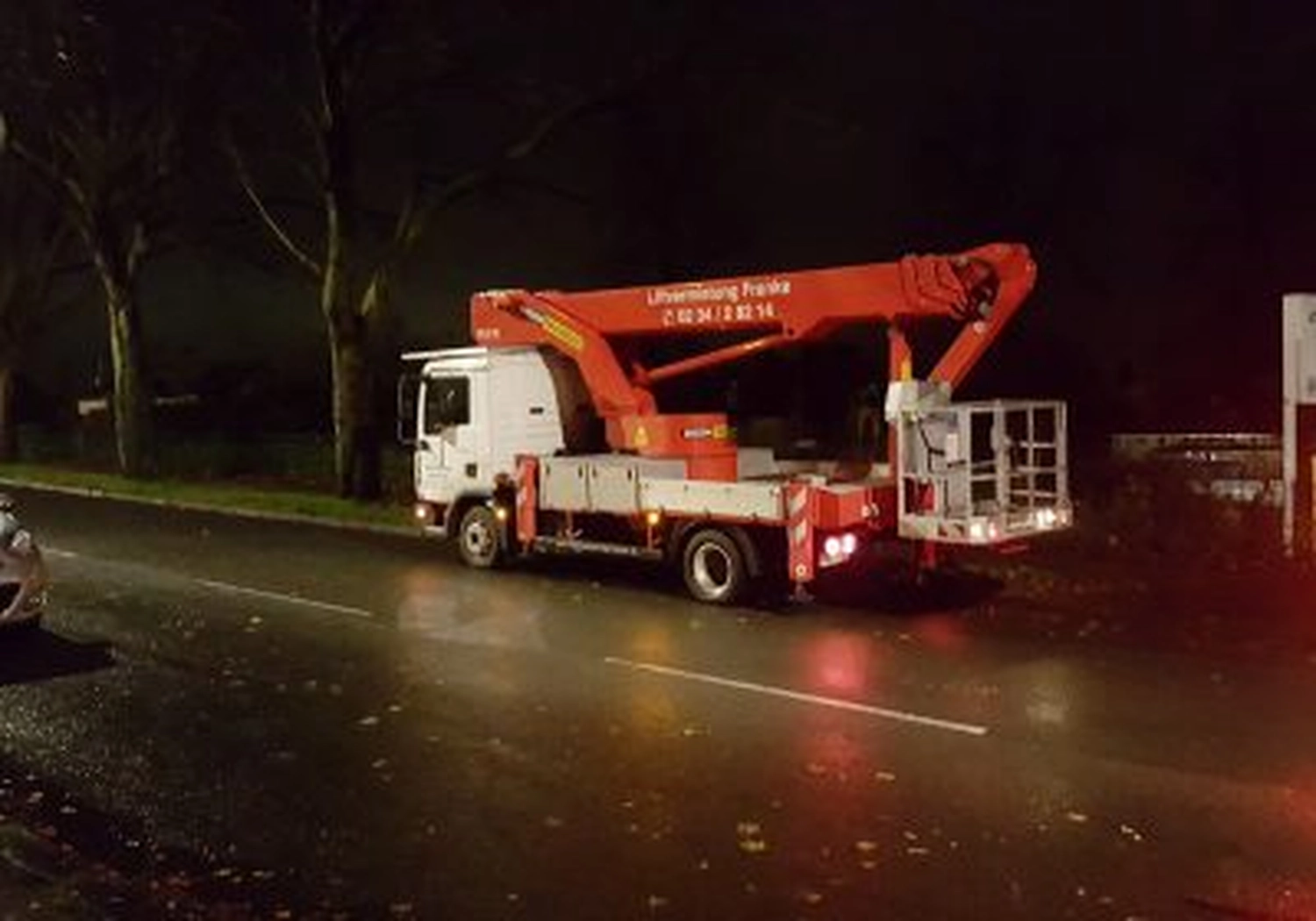 Tierschutzorganisation Arche 90 e.V. - Ein großer rot-weißer Rettungswagen mit ausgefahrenem Kranarm steht nachts auf einer nassen, dunklen Asphaltstraße.