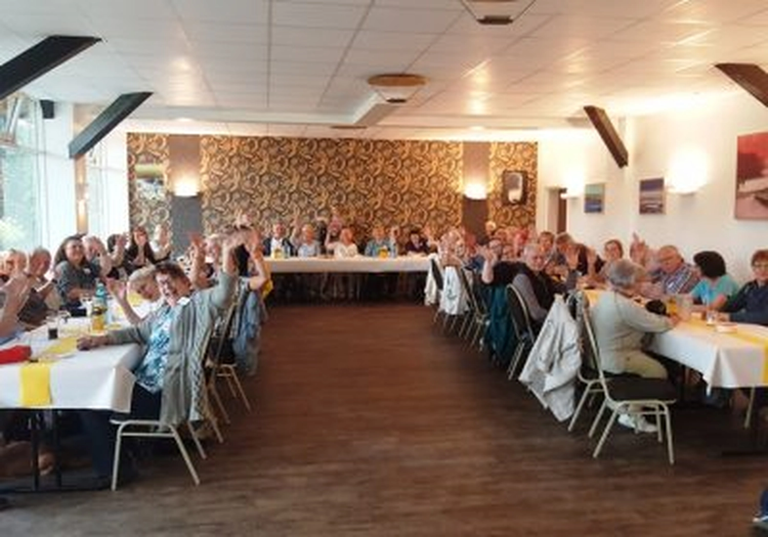 Tierschutzorganisation Arche 90 e.V. - Ein langer Festsaal mit Gästen an Tischen, die bei einem Treffen in geschlossenen Räumen anstoßen.