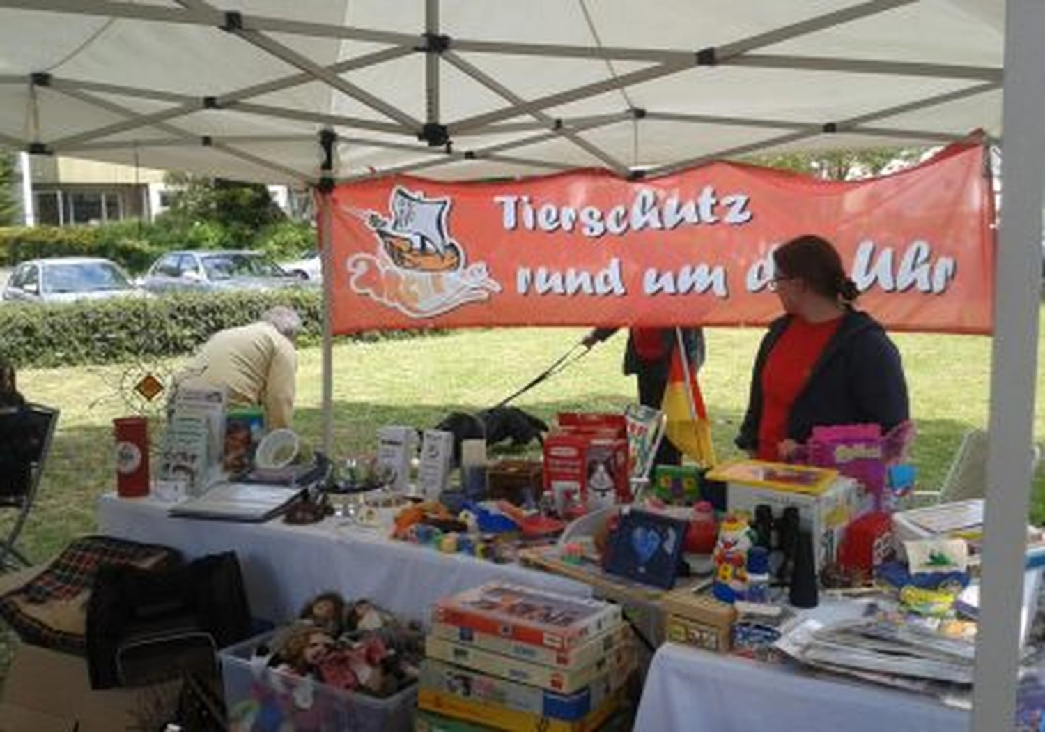 Tierschutzorganisation Arche 90 e.V. - Ein Stand bei einer Gemeinschaftsveranstaltung im Freien mit einem roten Banner mit der Aufschrift „Tierschutz rund um die Uhr“.